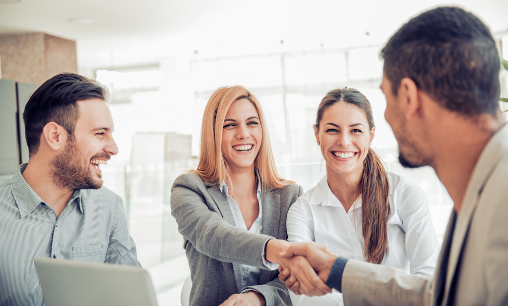 Two women and two men in business setting shaking hands